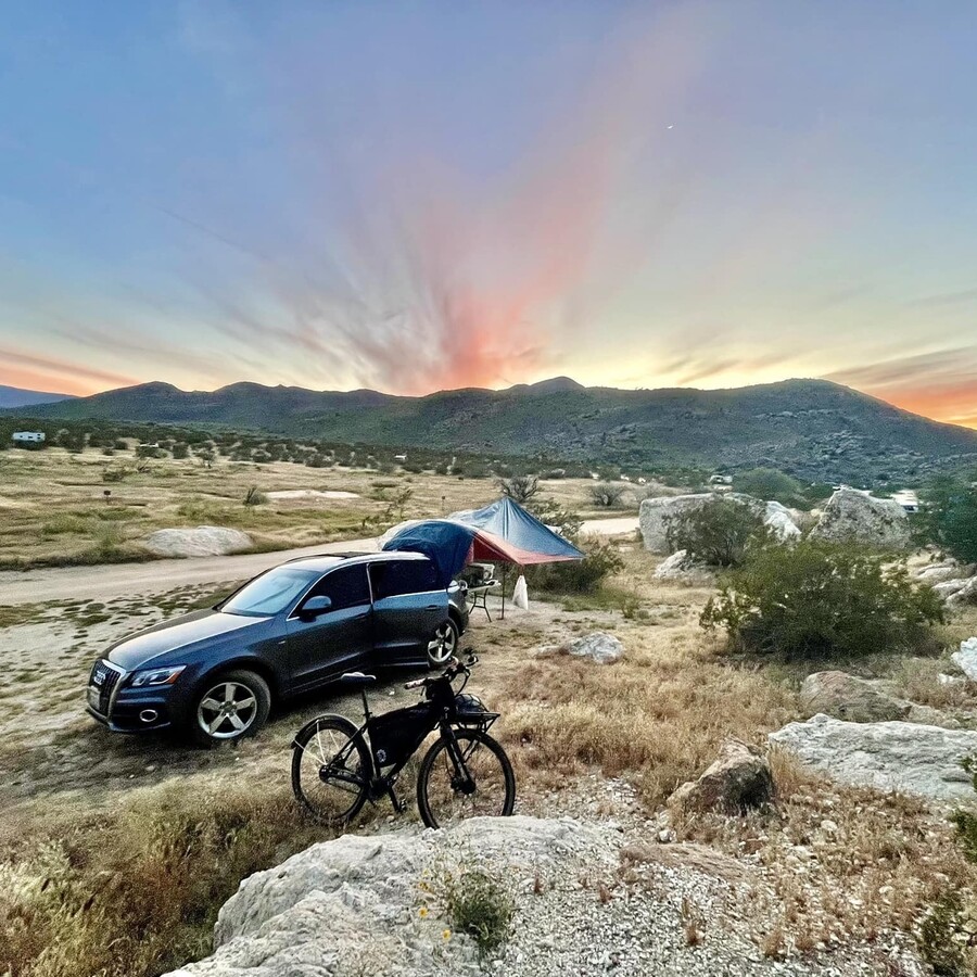 Car parked in the desert with mountains behind it and sunset colors above