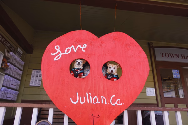 Two little dogs poking their heads out of the holes in a wooden heart