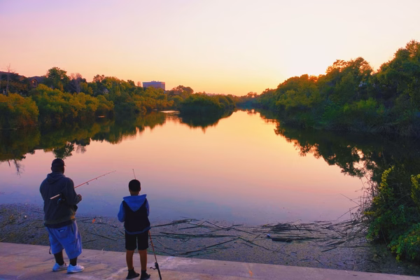 A man and boy fishing on the banks of a calm river